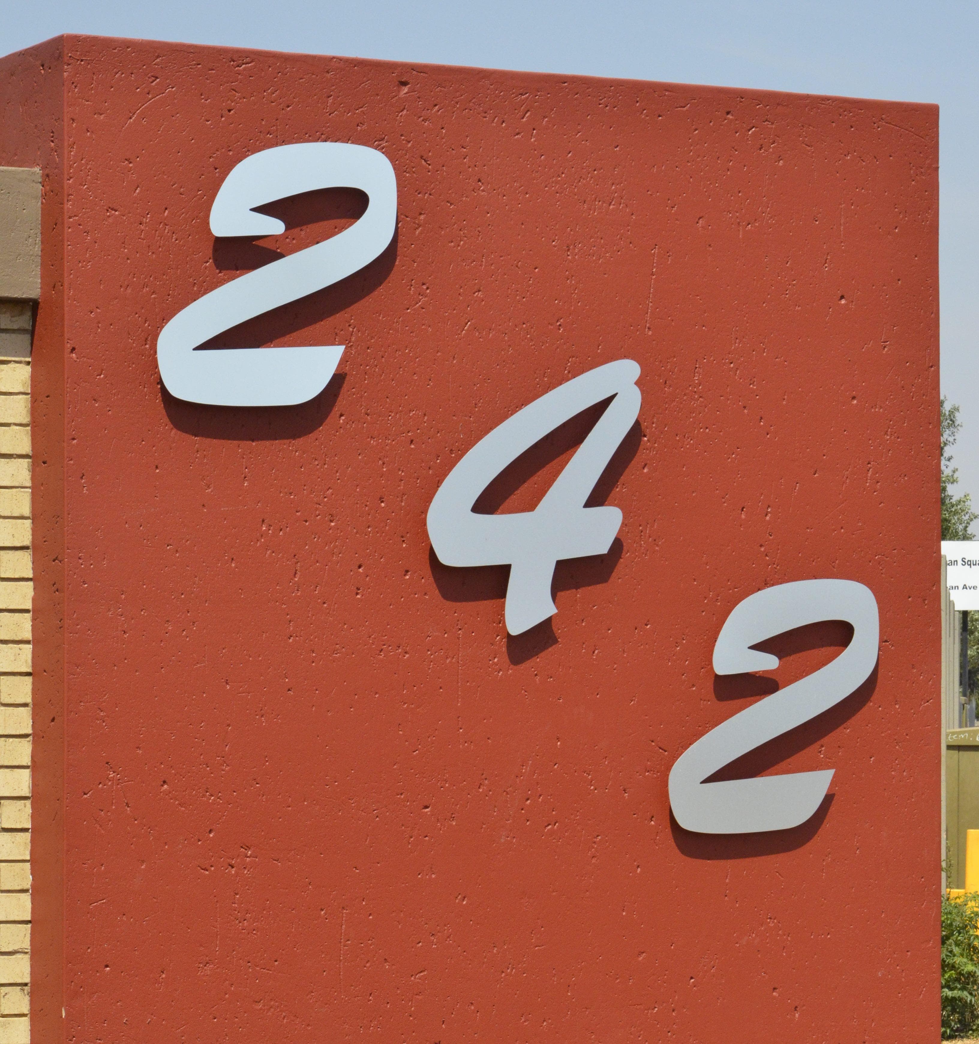 Large silver 242 street numbers mounted on a red plastered pillar