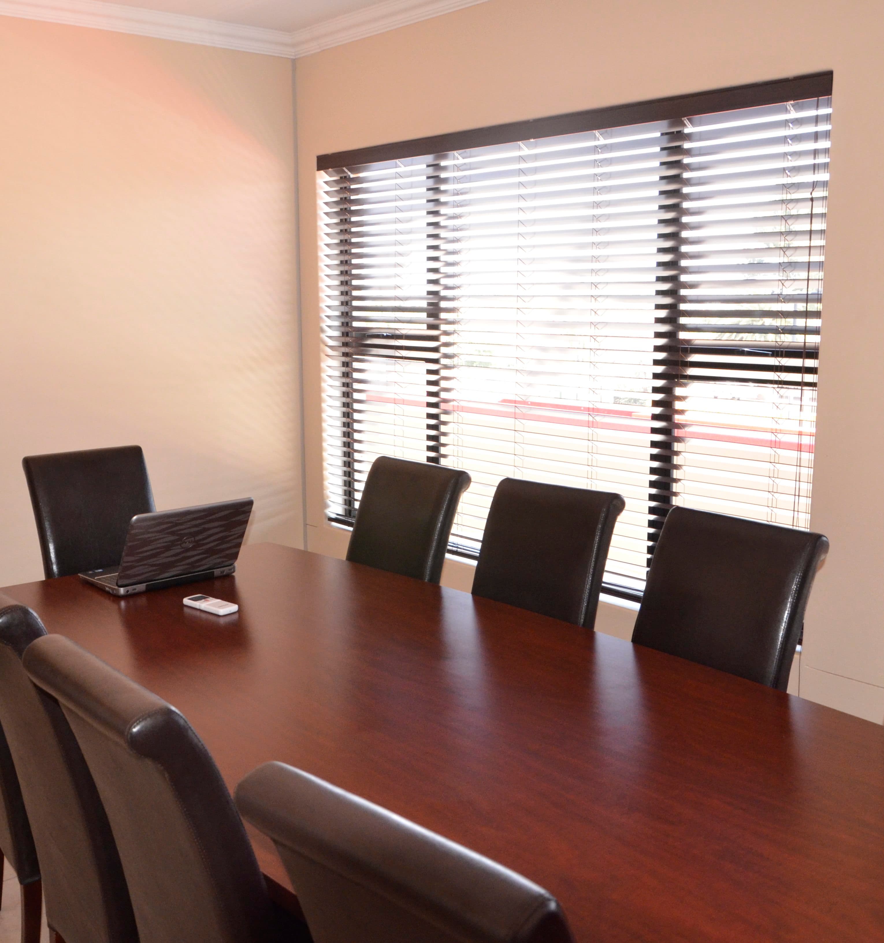 Conference table and leather chairs beside a large window with wooden blinds